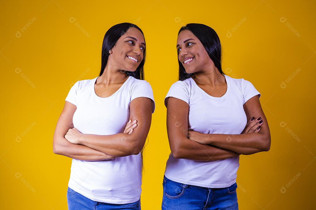 irmãs gêmeas idênticas em fundo amarelo com os braços cruzados