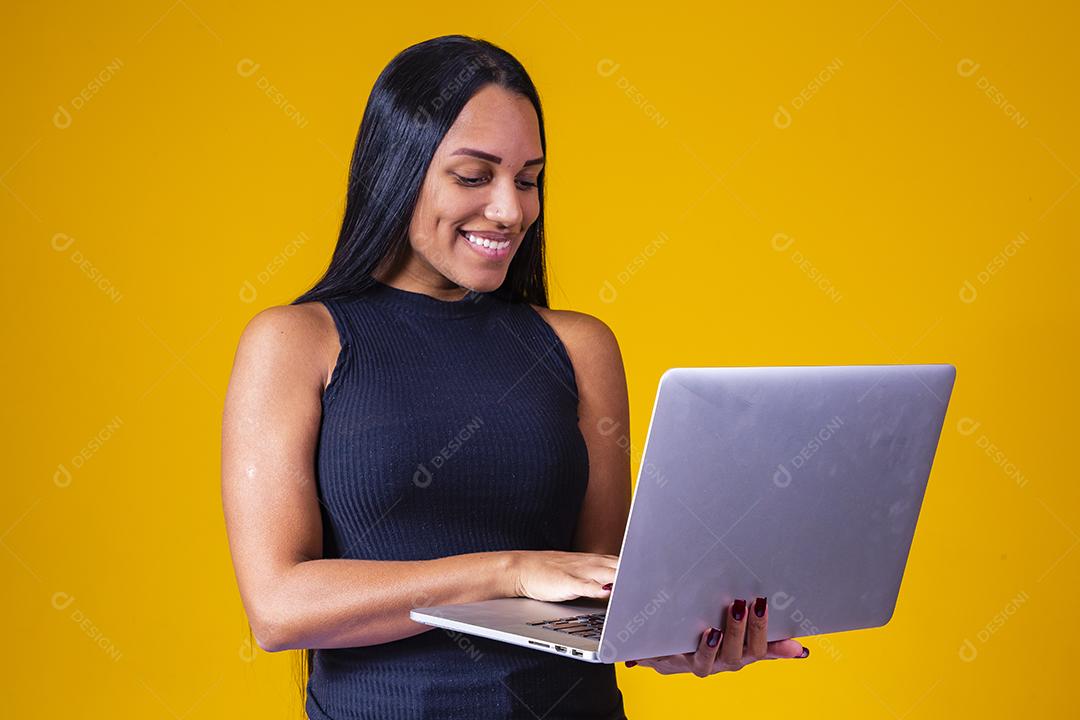 Mulher de negócios adulta feliz em vestido elegante, olhando para a câmera enquanto trabalhava no laptop contra fundo amarelo