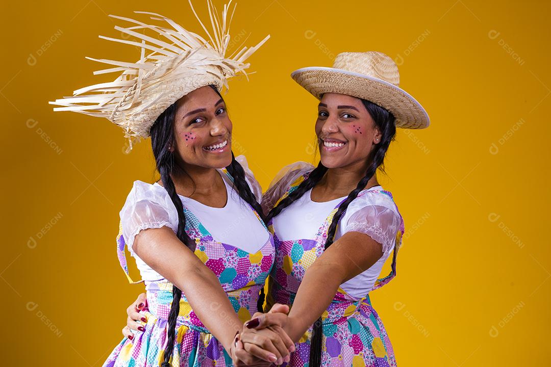 lindas irmãs gêmeas vestindo roupas tradicionais para festa de junho dançando em fundo amarelo