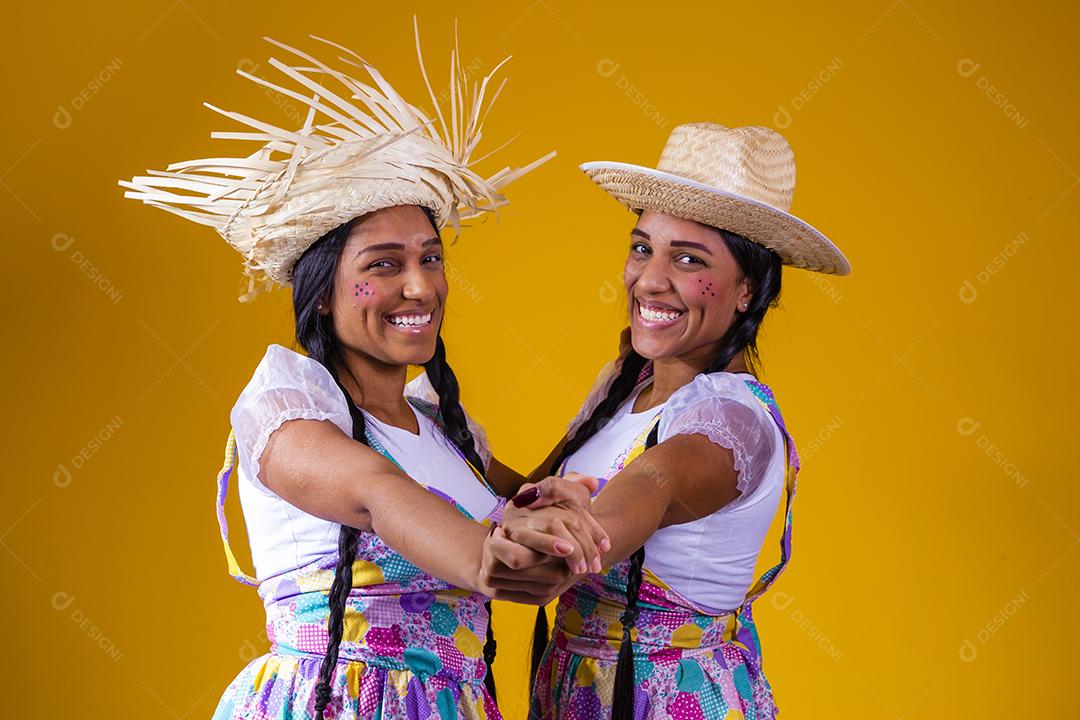 lindas irmãs gêmeas vestindo roupas tradicionais para festa de junho dançando em fundo amarelo