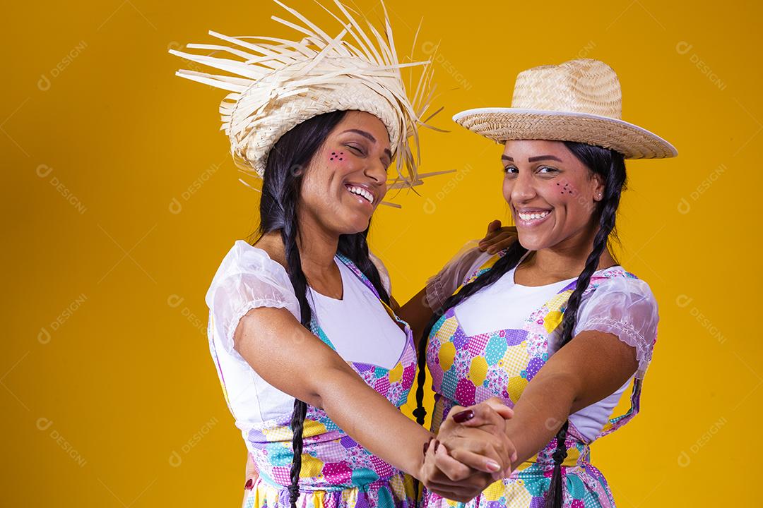 lindas irmãs gêmeas vestindo roupas tradicionais para festa de junho dançando em fundo amarelo