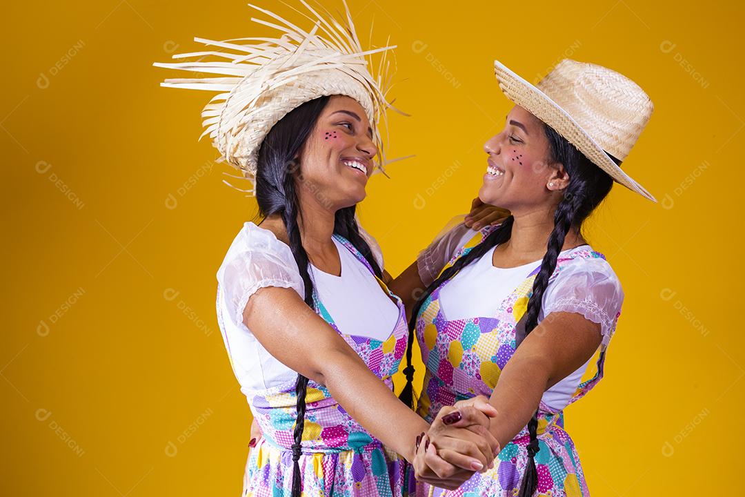lindas irmãs gêmeas vestindo roupas tradicionais para festa de junho dançando em fundo amarelo