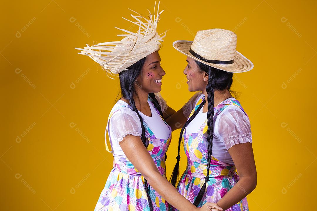 lindas irmãs gêmeas vestindo roupas tradicionais para festa de junho dançando em fundo amarelo