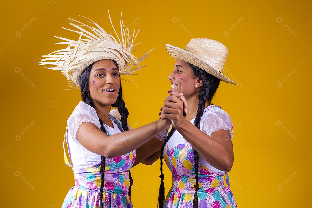 lindas irmãs gêmeas vestindo roupas tradicionais para festa de junho dançando em fundo amarelo