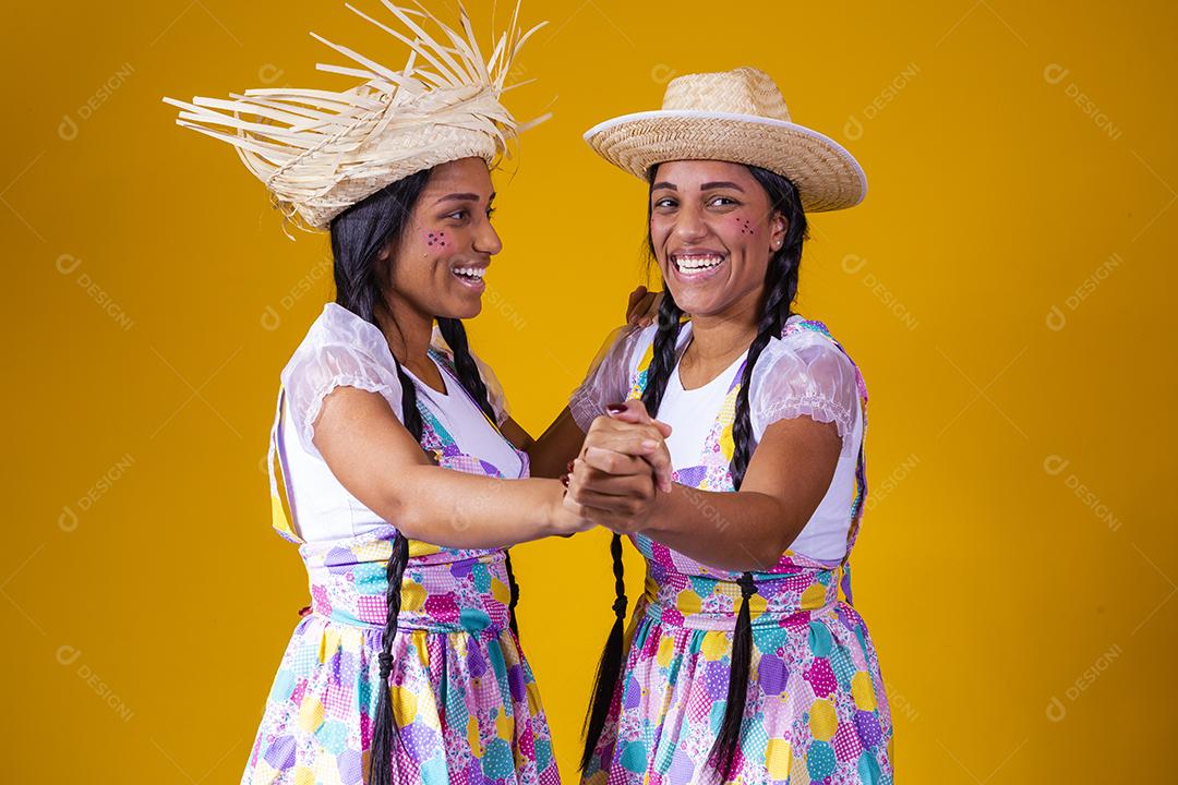 lindas irmãs gêmeas vestindo roupas tradicionais para festa de junho dançando em fundo amarelo