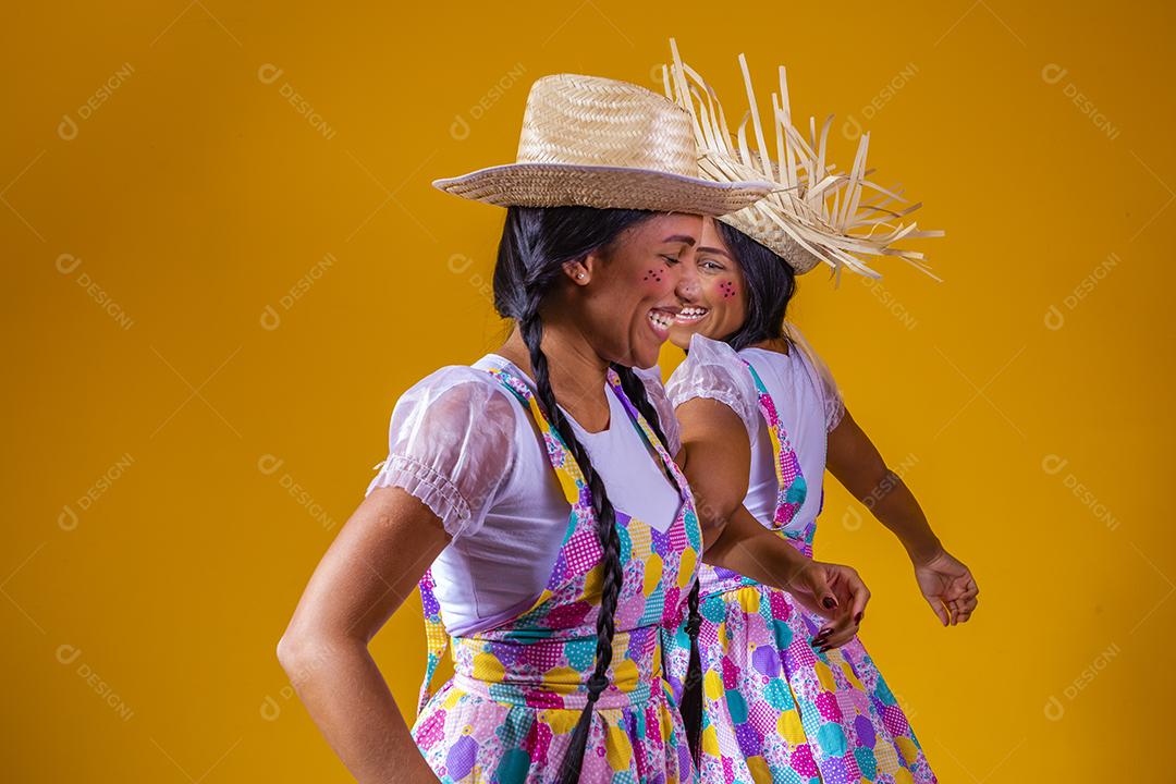 lindas irmãs gêmeas vestindo roupas tradicionais para festa de junho dançando em fundo amarelo