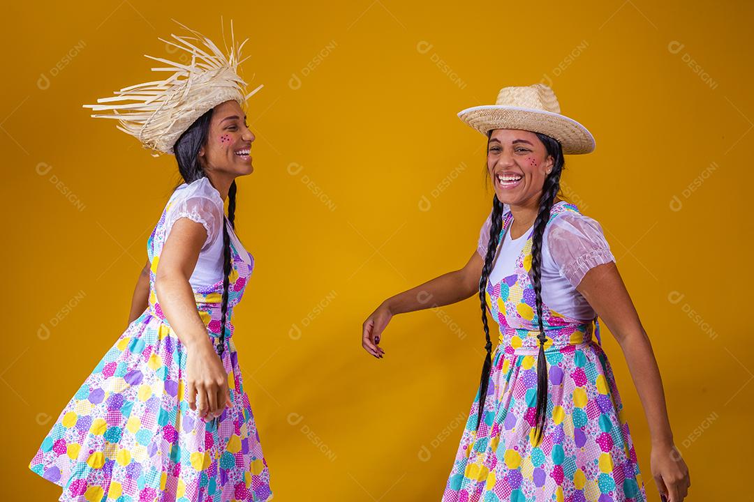 lindas irmãs gêmeas vestindo roupas tradicionais para festa de junho dançando em fundo amarelo