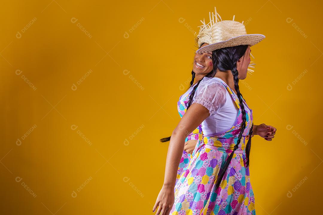 lindas irmãs gêmeas vestindo roupas tradicionais para festa de junho dançando em fundo amarelo