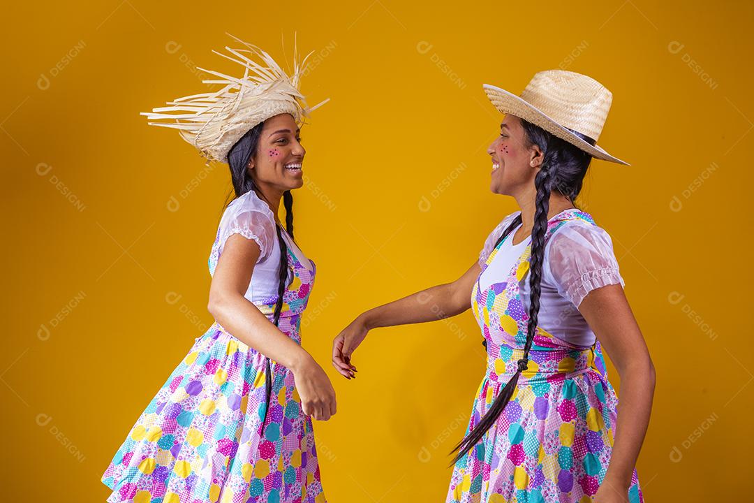 lindas irmãs gêmeas vestindo roupas tradicionais para festa de junho dançando em fundo amarelo