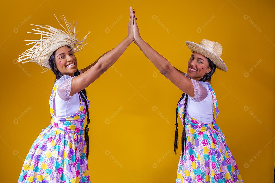 lindas irmãs gêmeas vestindo roupas tradicionais para festa de junho dançando em fundo amarelo