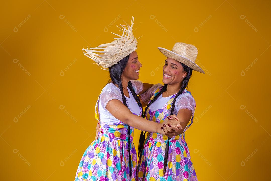 Lindas irmãs gêmeas vestindo roupas tradicionais para festa de junho dançando em fundo amarelo