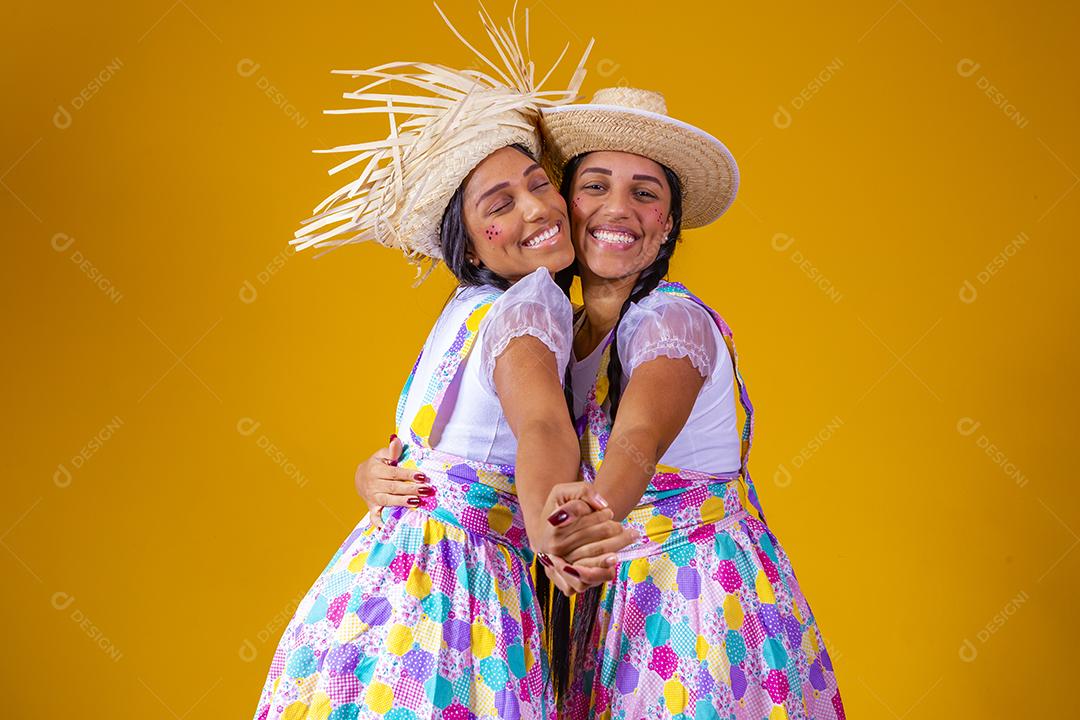 Lindas irmãs gêmeas vestindo roupas tradicionais para festa de junho dançando em fundo amarelo