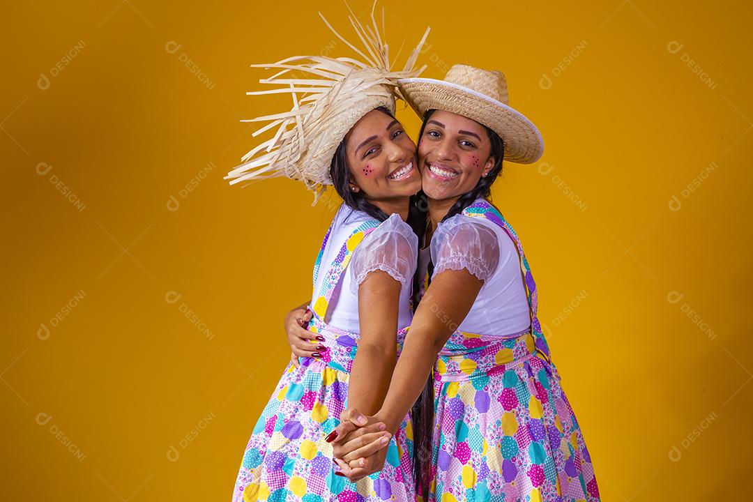 Lindas irmãs gêmeas vestindo roupas tradicionais para festa de junho dançando em fundo amarelo
