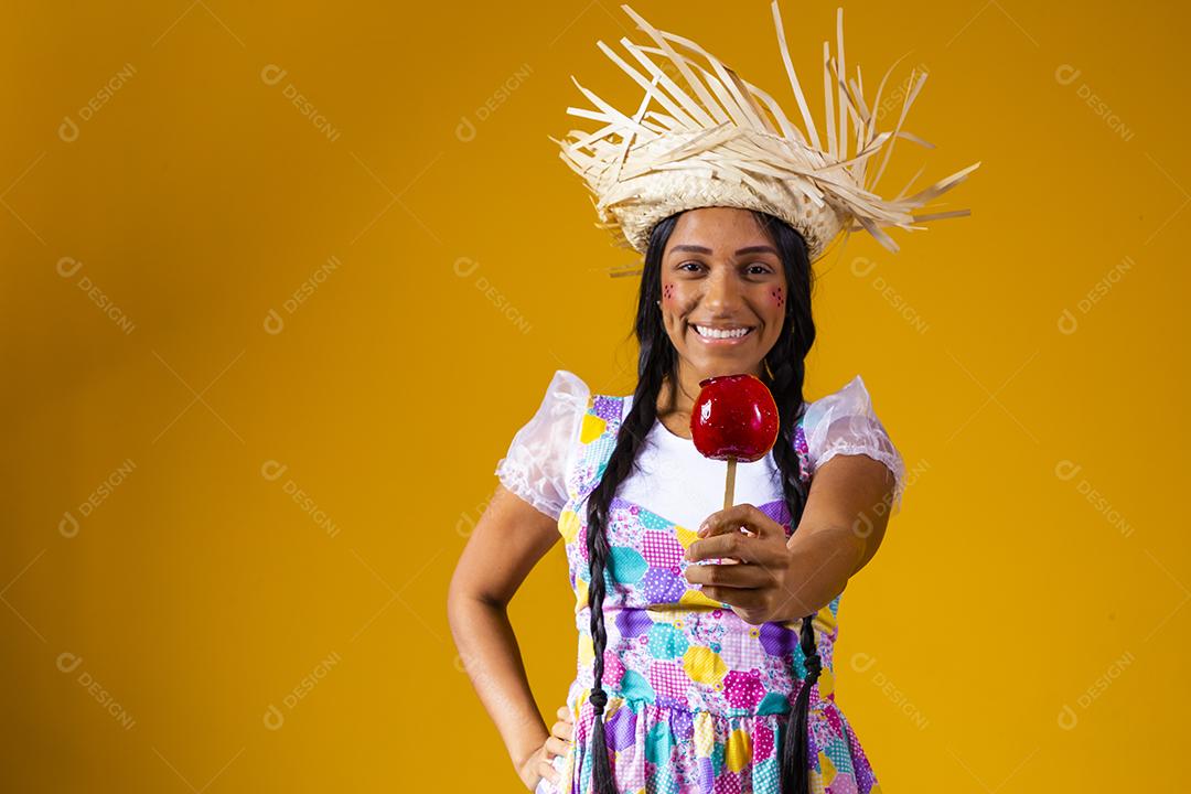 Mulher jovem e bonita em roupas de festa de junho comendo a maçã do amor. Sobremesa de maçã coberta de caramelo vermelho