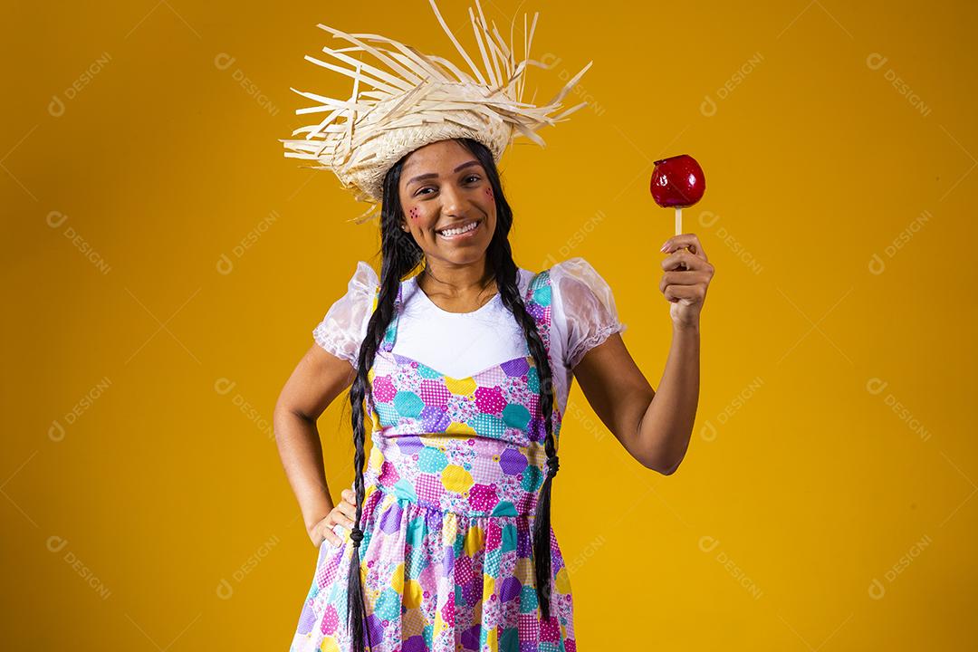 Mulher jovem e bonita em roupas de festa de junho comendo a maçã do amor. Sobremesa de maçã coberta de caramelo vermelho