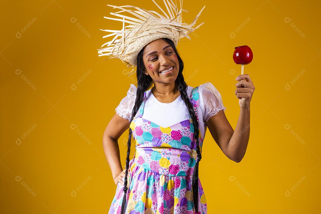 Mulher jovem e bonita em roupas de festa de junho comendo a maçã do amor. Sobremesa de maçã coberta de caramelo vermelho