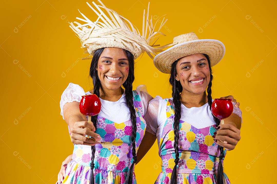 Lindas garotas gêmeas em roupas de festa junina comendo uma maçã caramelada