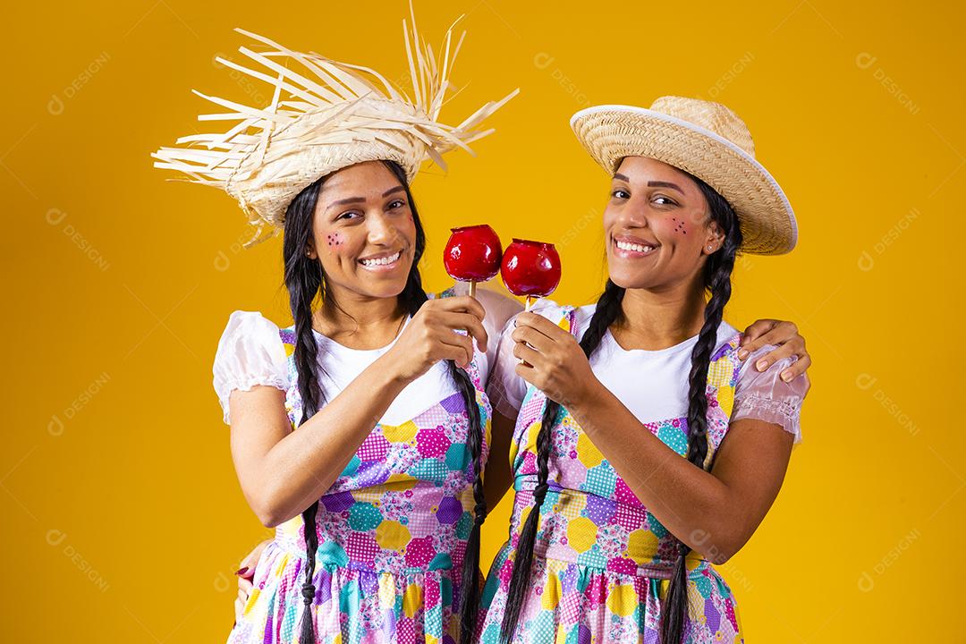 Lindas garotas gêmeas em roupas de festa junina comendo uma maçã caramelada