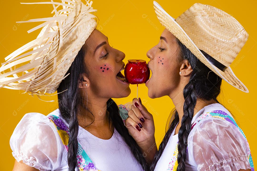 Lindas garotas gêmeas em roupas de festa junina comendo uma maçã caramelada