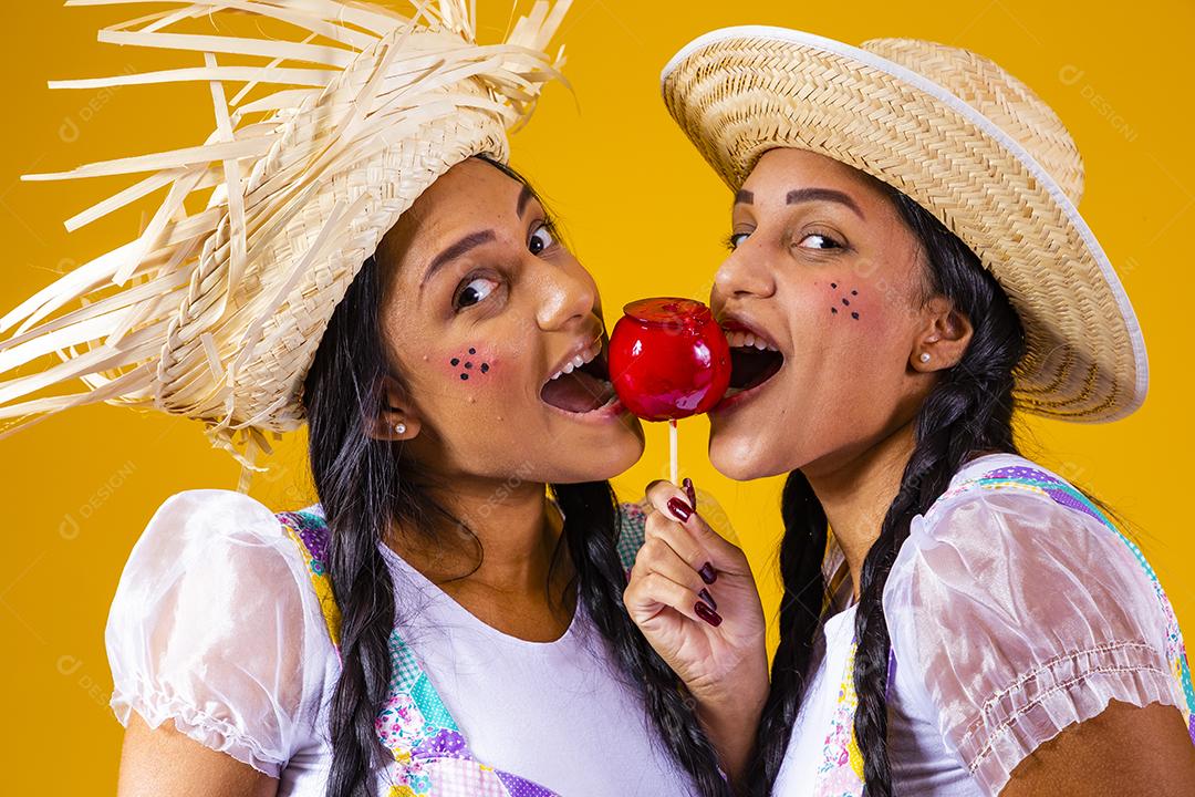Lindas garotas gêmeas em roupas de festa junina comendo uma maçã caramelada