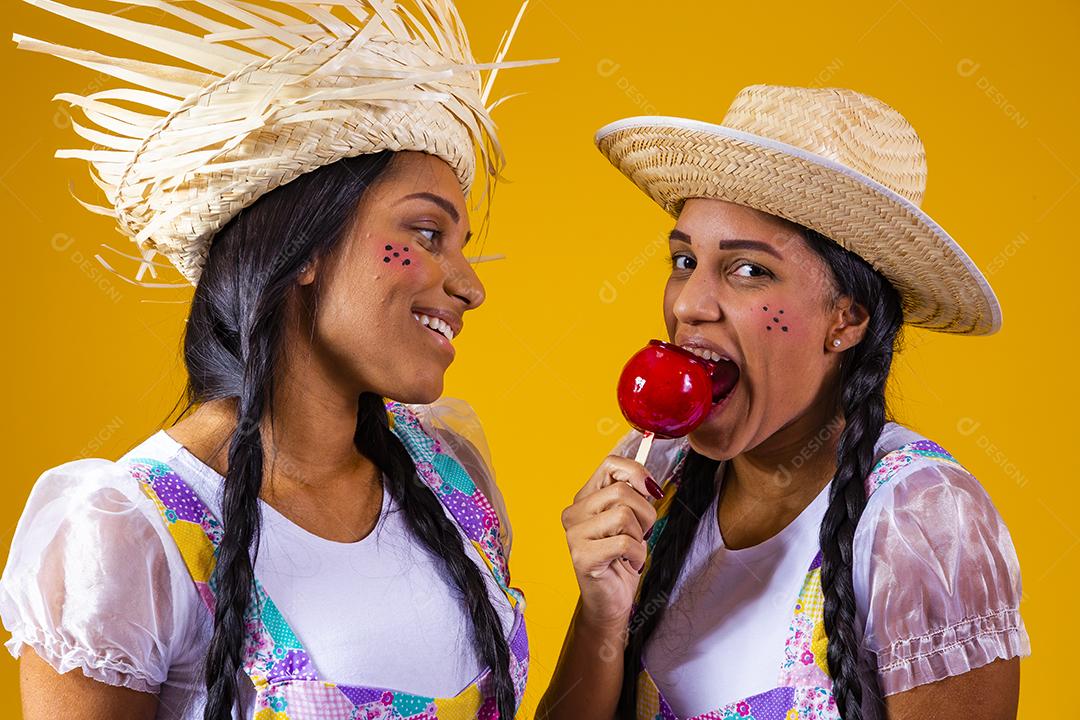 Lindas garotas gêmeas em roupas de festa junina comendo uma maçã caramelada