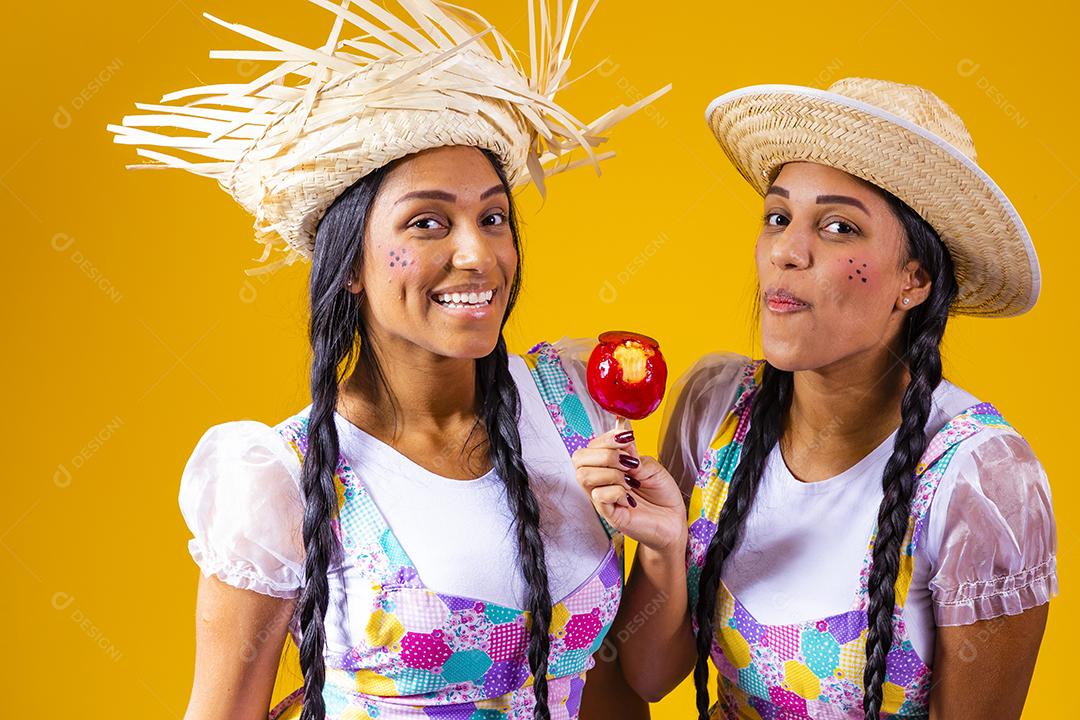 Lindas garotas gêmeas em roupas de festa junina comendo uma maçã caramelada