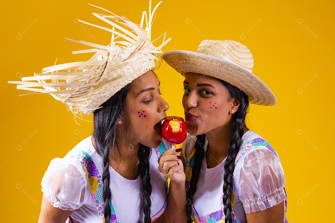 Lindas garotas gêmeas em roupas de festa junina comendo uma maçã caramelada