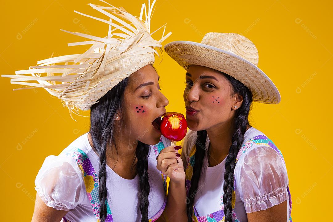 Lindas garotas gêmeas em roupas de festa junina comendo uma maçã caramelada