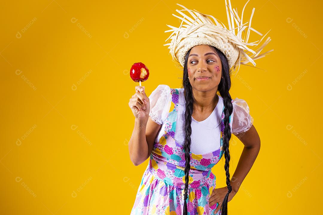 Mulher jovem e bonita em roupas de festa de junho comendo a maçã do amor. Sobremesa de maçã coberta de caramelo vermelho