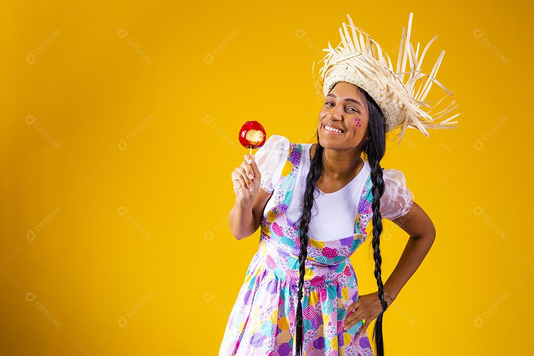 Mulher jovem e bonita em roupas de festa de junho comendo a maçã do amor. Sobremesa de maçã coberta de caramelo vermelho