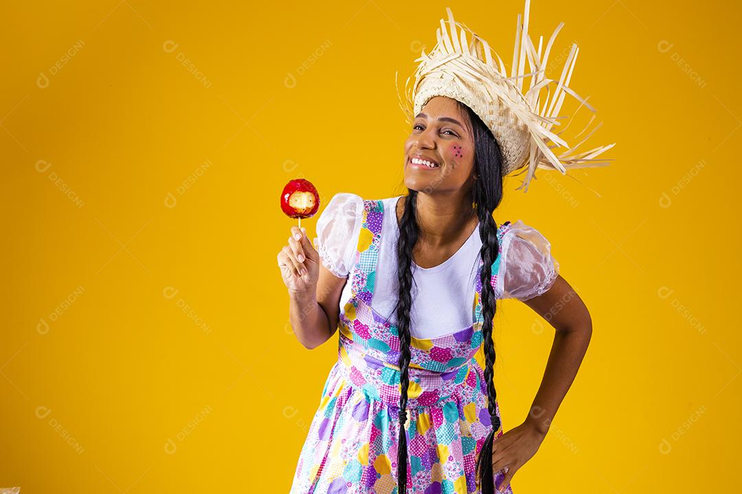 Mulher jovem e bonita em roupas de festa de junho comendo a maçã do amor. Sobremesa de maçã coberta de caramelo vermelho