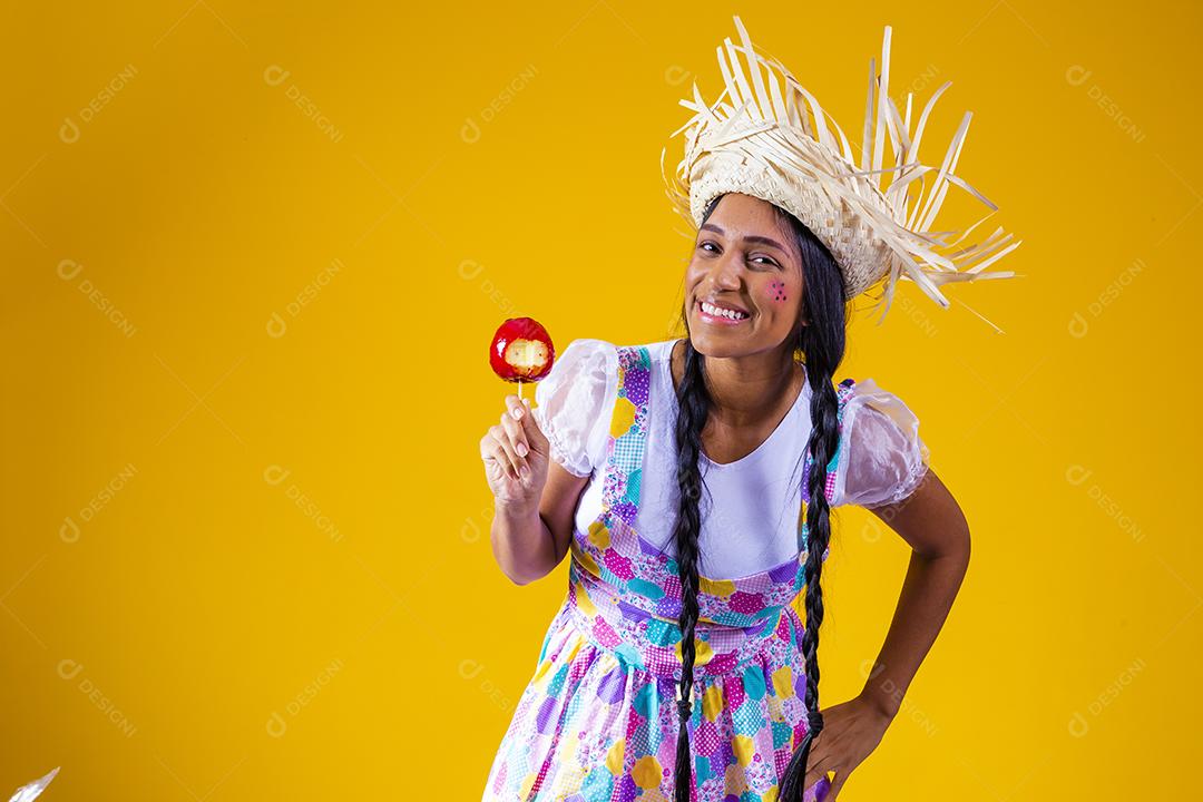 Mulher jovem e bonita em roupas de festa de junho comendo a maçã do amor. Sobremesa de maçã coberta de caramelo vermelho