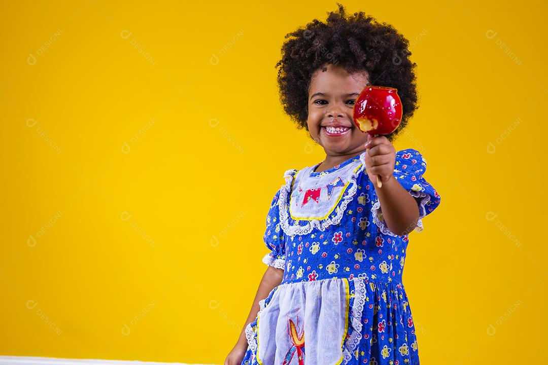 Adorável menina negra vestida com roupas de festa de junho comendo a maçã do amor. Sobremesa de maçã