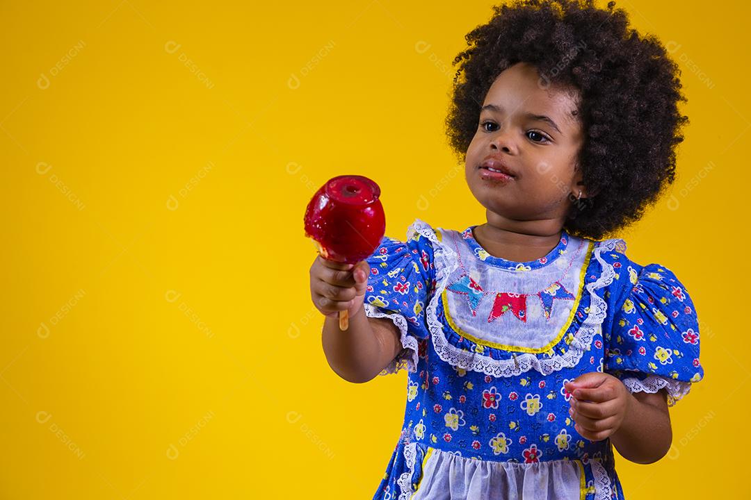 Adorável menina negra vestida com roupas de festa de junho comendo a maçã do amor. Sobremesa de maçã