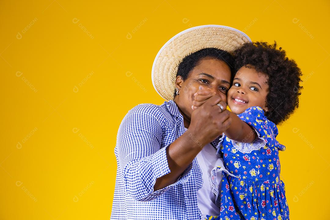 mãe e filha afro vestindo roupas tradicionais para Festa Junina dançando em fundo amarelo