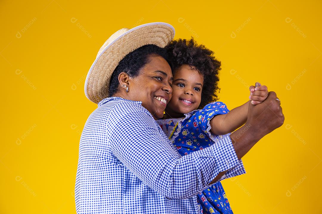 mãe e filha afro vestindo roupas tradicionais para Festa Junina dançando em fundo amarelo