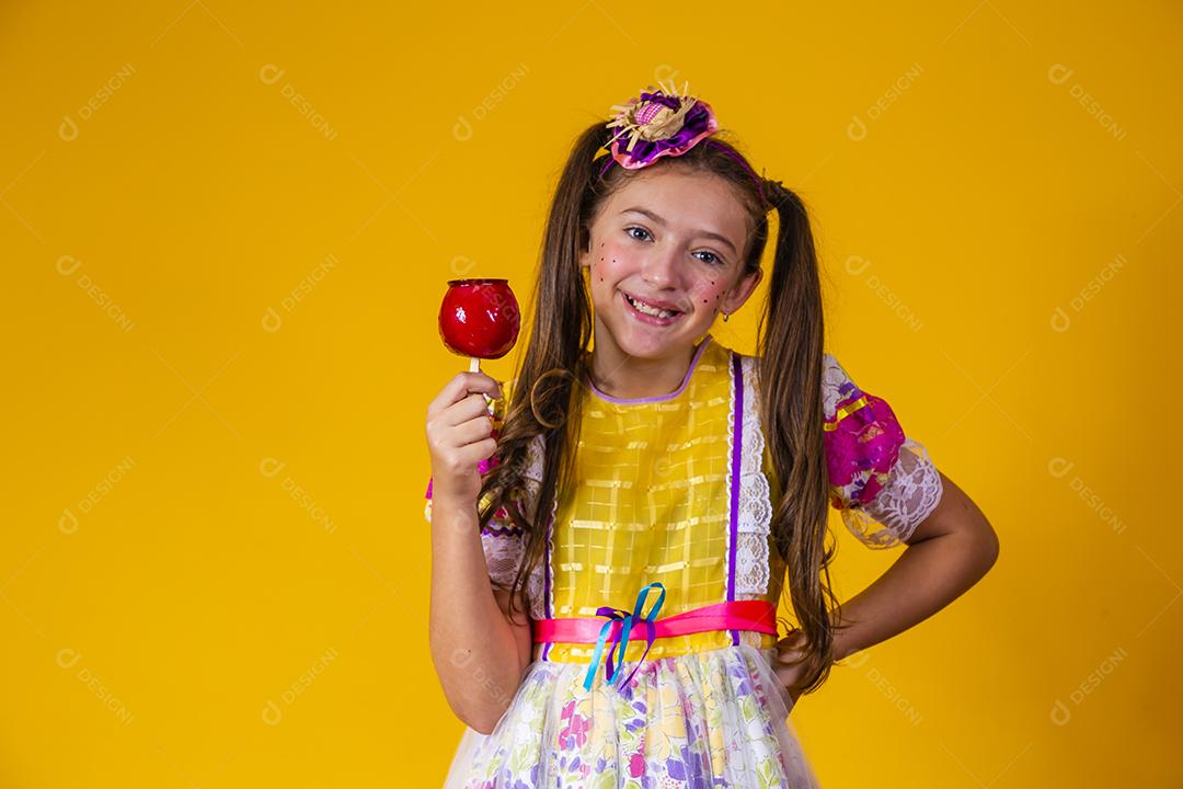 Linda garota com roupas de festa de junho comendo a maçã do amor. Sobremesa de maçã coberta de caramelo vermelho