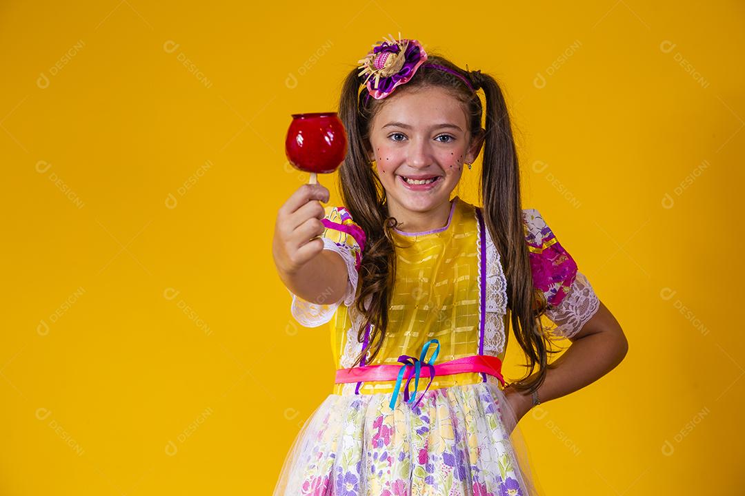 Linda garota com roupas de festa de junho comendo a maçã do amor. Sobremesa de maçã coberta de caramelo vermelho