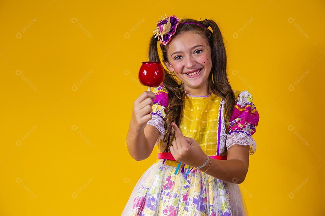 Linda garota com roupas de festa de junho comendo a maçã do amor. Sobremesa de maçã coberta de caramelo vermelho