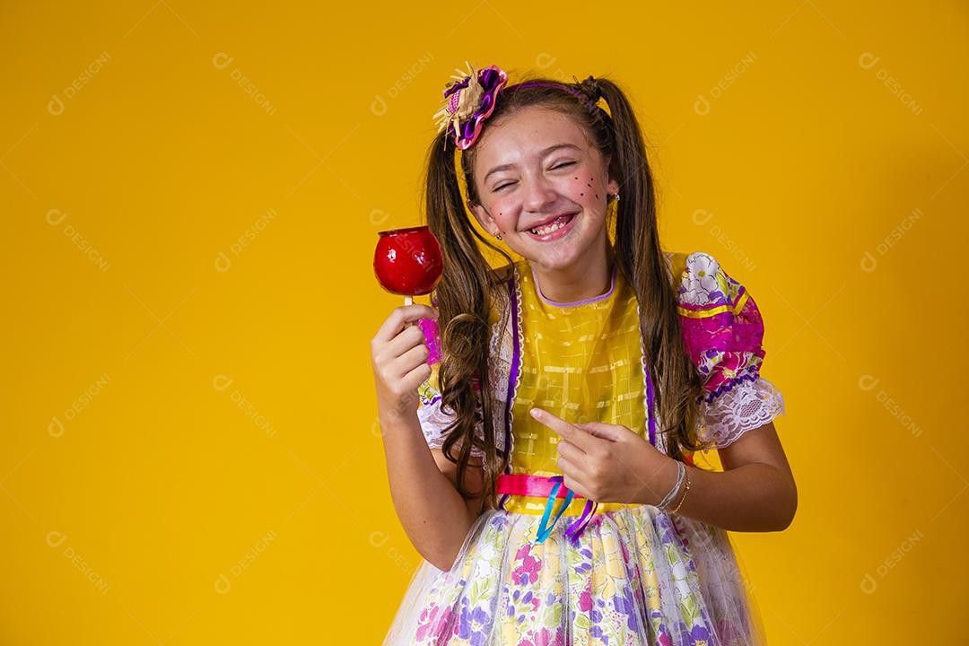 Linda garota com roupas de festa de junho comendo a maçã do amor. Sobremesa de maçã coberta de caramelo vermelho