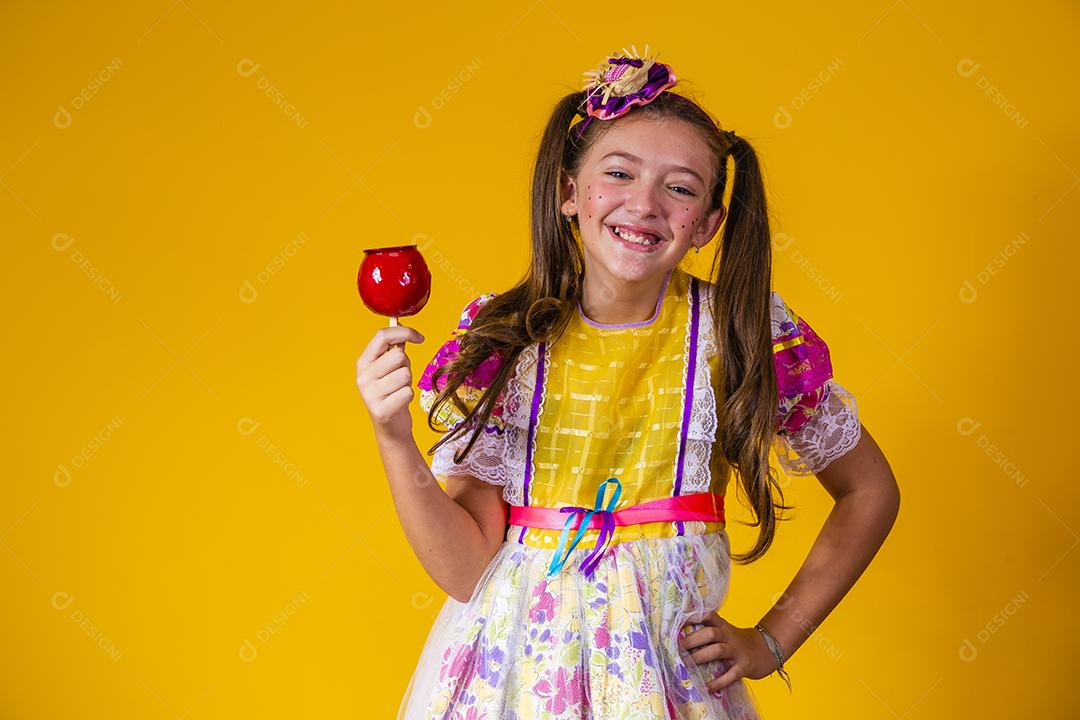 Linda garota com roupas de festa de junho comendo a maçã do amor. Sobremesa de maçã coberta de caramelo vermelho