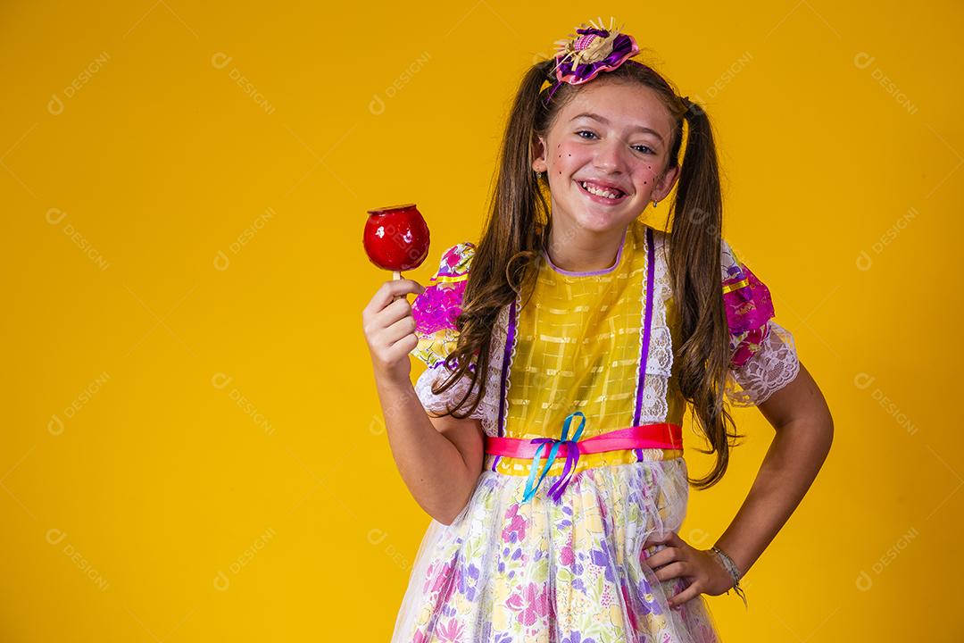 Linda garota com roupas de festa de junho comendo a maçã do amor. Sobremesa de maçã coberta de caramelo vermelho