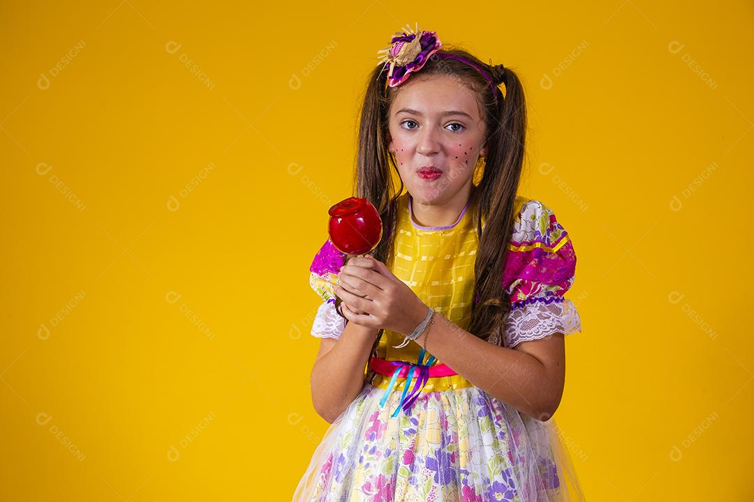 Linda garota com roupas de festa de junho comendo a maçã do amor. Sobremesa de maçã coberta de caramelo vermelho