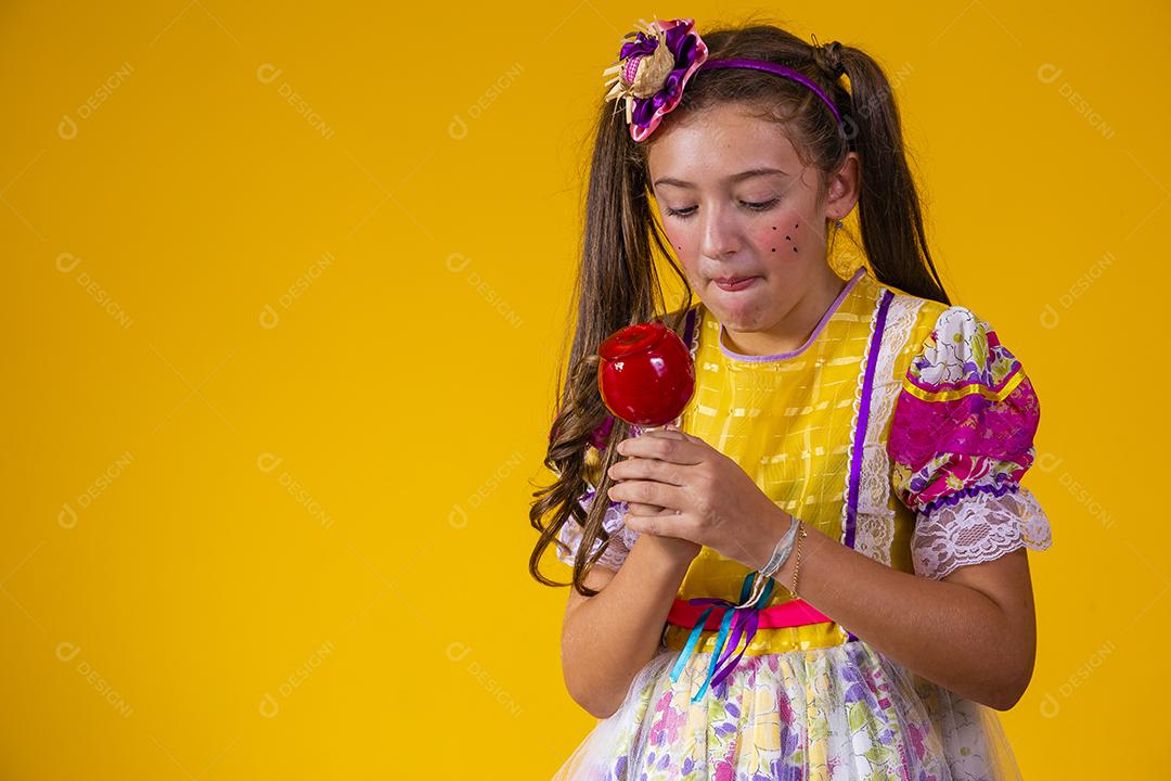 Linda garota com roupas de festa de junho comendo a maçã do amor. Sobremesa de maçã coberta de caramelo vermelho