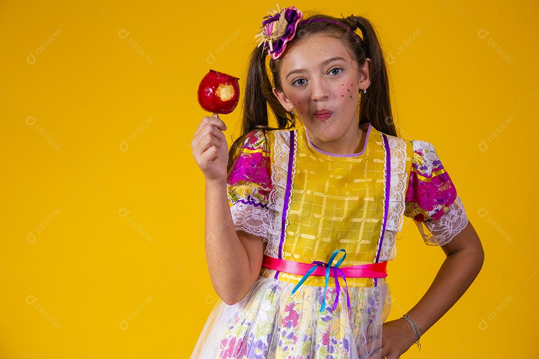 Linda garota caucasiana com roupa típica de festa junina comendo maçã com caramelo.
