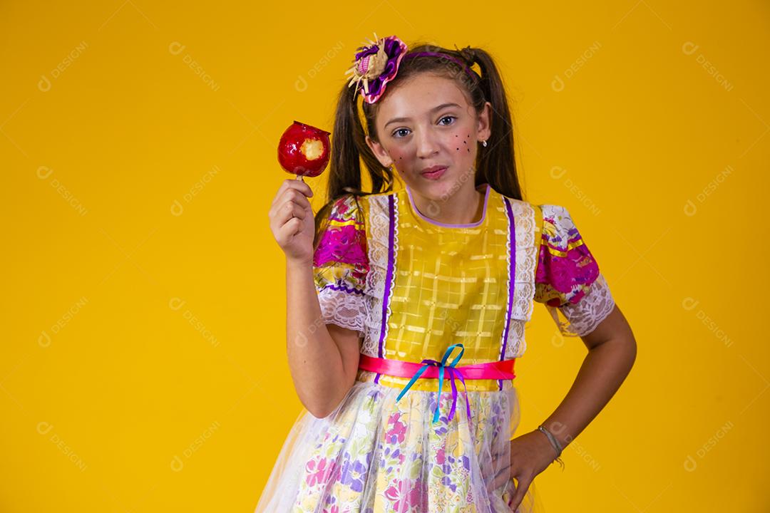 Linda garota caucasiana com roupa típica de festa junina comendo maçã com caramelo.