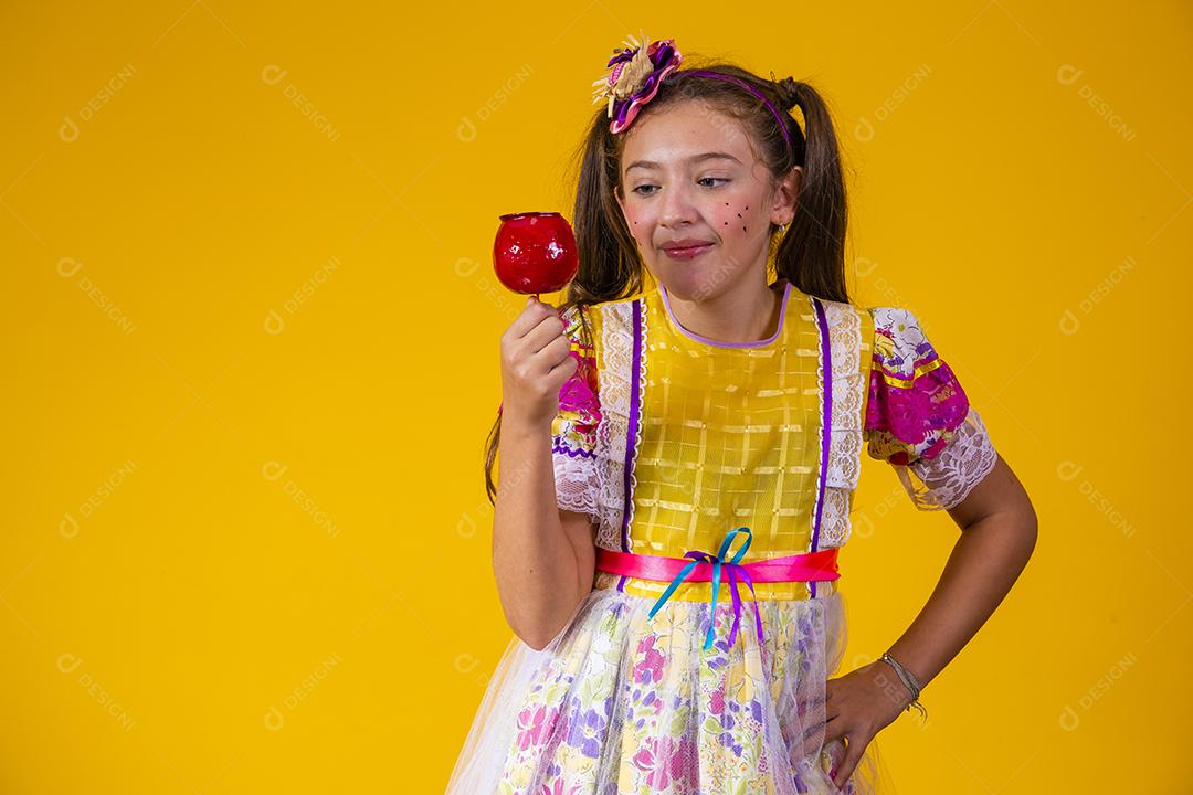 Linda garota caucasiana com roupa típica de festa junina comendo maçã com caramelo.