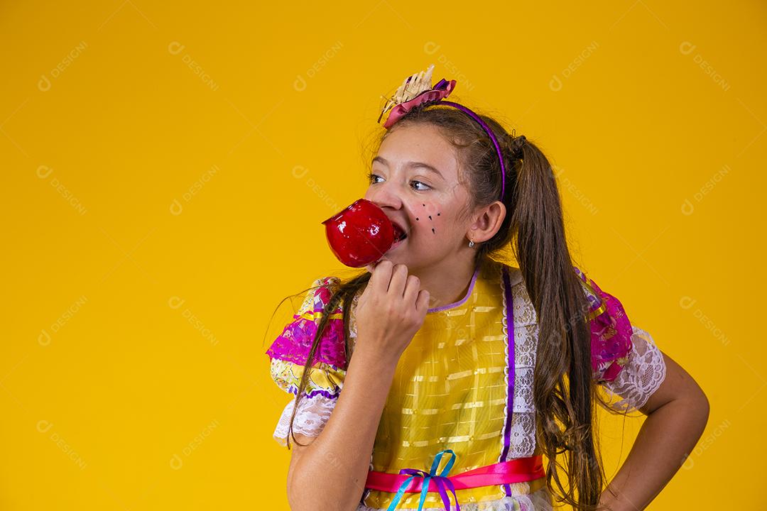 Linda garota caucasiana com roupa típica de festa junina comendo maçã com caramelo.