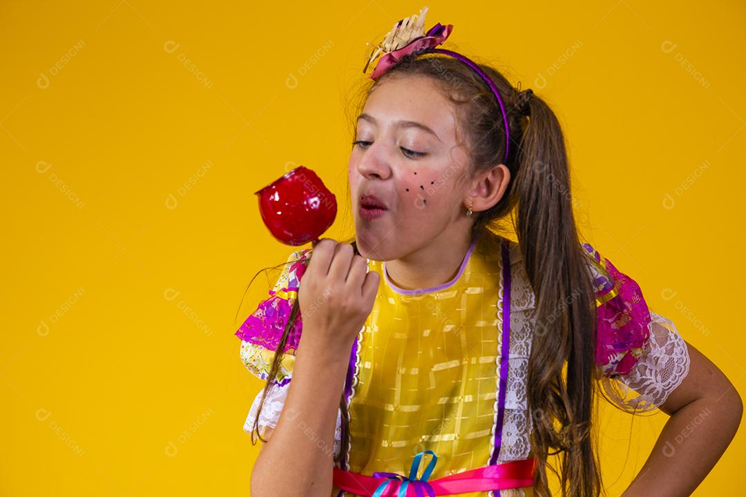 Linda garota caucasiana com roupa típica de festa junina comendo maçã com caramelo.