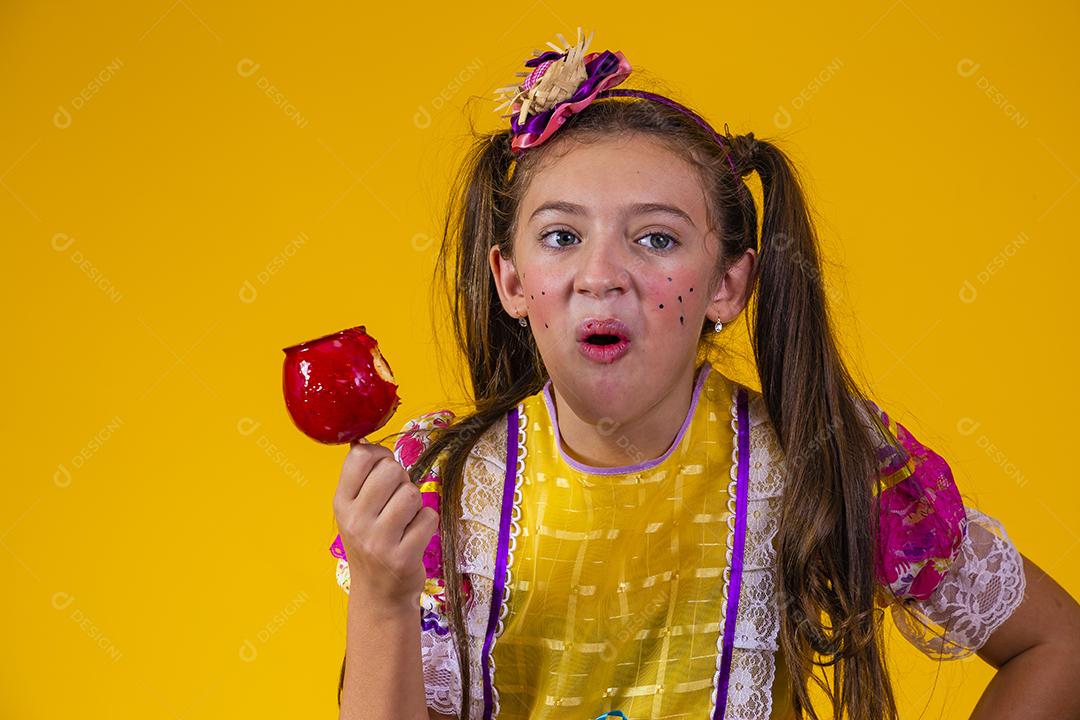 Linda garota caucasiana com roupa típica de festa junina comendo maçã com caramelo.